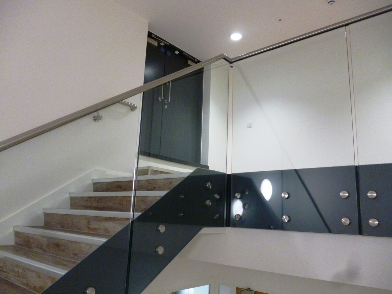 Staircase with glass balustrade and brushed metal handrail, blending safety with modern style.