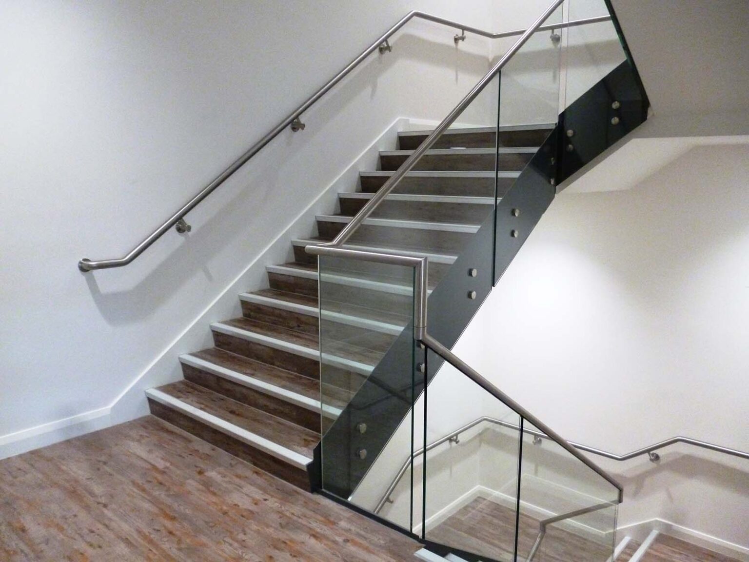 Contemporary staircase with glass panels and sleek handrail, combining wood and metal elements.
